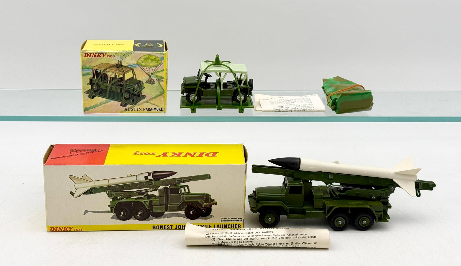 A Pair of Vintage Dinky Toys Military Vehicle Boxed Sets: Dinky Toys Austin Para-Moke No. 601 and Honest John Missile Launcher No. 665, both constructed from olive drab die-cast metal. The Para-Moke set includes a detachable assault platform and a packaged c