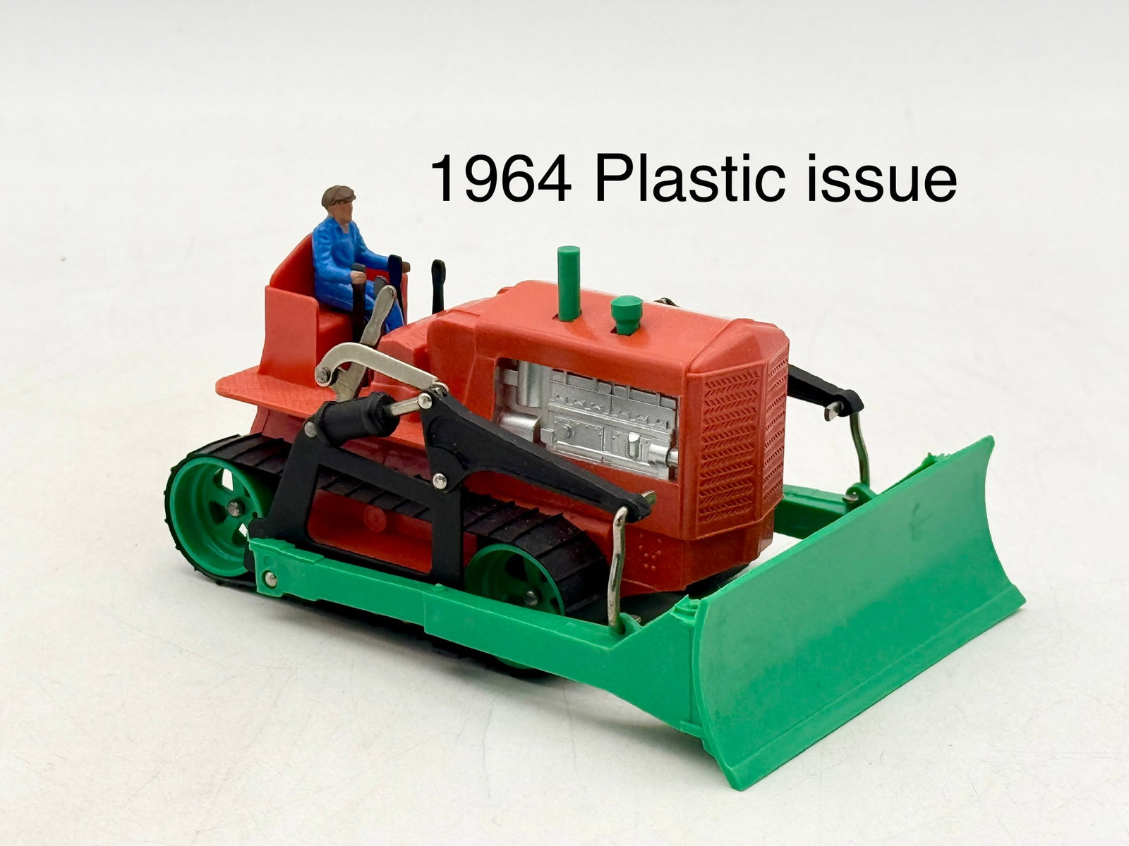 Dinky Supertoys 961 Plastic Blaw Knox Bulldozer with Driver: This Dinky Supertoys model 961 is a molded plastic Blaw Knox bulldozer produced by Meccano Ltd. in England. The model features a red body with a green front blade, green wheels, black tracks, and a se