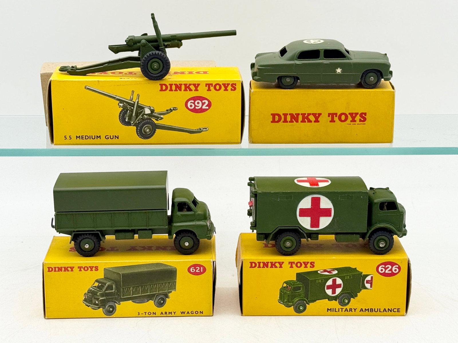 A Collection of Vintage Dinky Toys Die-Cast Military Vehicles: This collection of Dinky Toys military vehicles and artillery, made in England by Meccano Ltd., includes a medium gun, army wagon, ambulance, and staff car. Each die-cast model is finished in olive dr