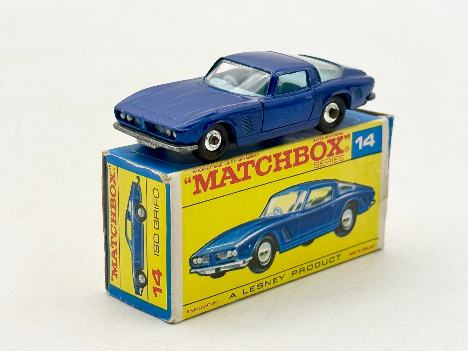 Matchbox Series No. 14D1 Iso Grifo with Original Box: A Matchbox Series No. 14D1 Iso Grifo die-cast model car by Lesney Products, finished in dark blue with clear glazing and a light blue plastic tow hook. The vehicle features an unpainted metal base emb