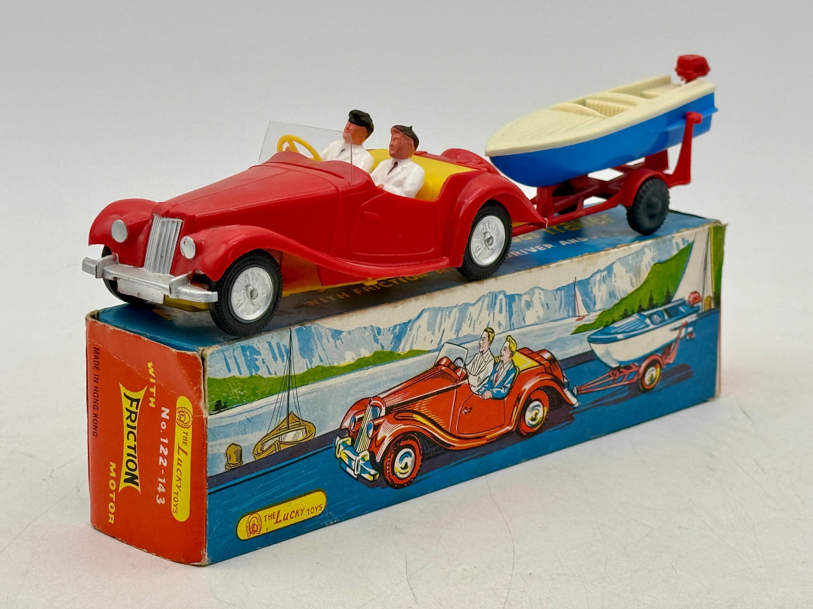 Lucky Toys M.G. Midget Sports Car and Boat Trailer Set: The Lucky Toys M.G. Midget sports car and boat trailer set is constructed of molded plastic and includes its original color-illustrated box. The friction-powered red roadster features a yellow interio