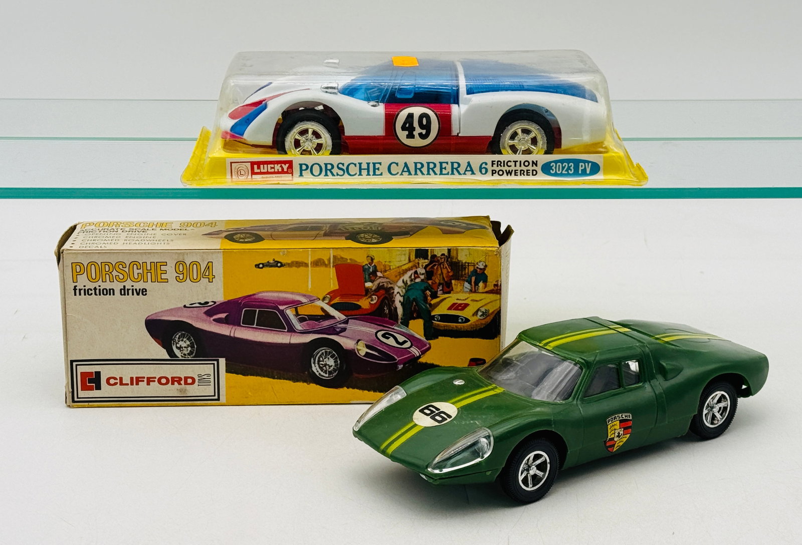 2 Vintage Porsche Friction Powered Toy Racing Cars one factory sealed: A pair of vintage Hong Kong plastic friction-drive models including a Lucky 1966 Porsche Carrera 6 (factory sealed) and a Clifford Toys 1964 Porsche 904. Both cars feature molded plastic bodies with c