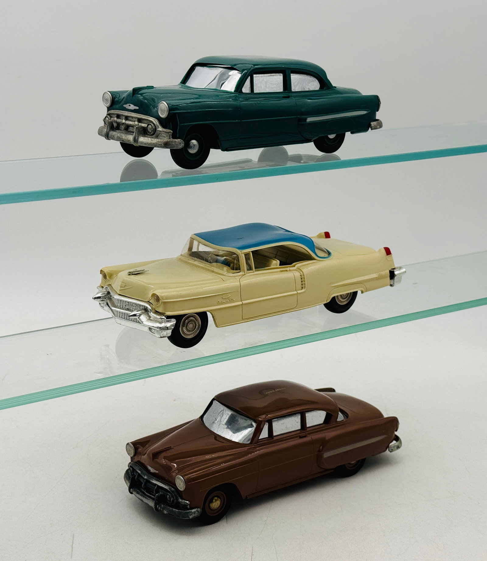 3 Mid-Century American Chevrolet and Cadillac Promo Toy Cars: 3 1950s free-wheeling promo toy cars is constructed of molded hard plastic with painted silver accents and trim. The collection includes two 1953-1954 Chevrolet four-door sedans in green and saddle br