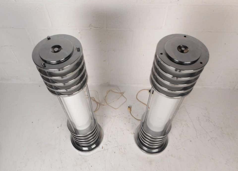 Pair of Vintage Art Deco Style Floor Lamps: This stunning pair of Art Deco style floor lamps stand 41 inches high and have a cylindrical body that lights up. This machine age pair feature wraparound chrome on the top and bottom as well as a stu