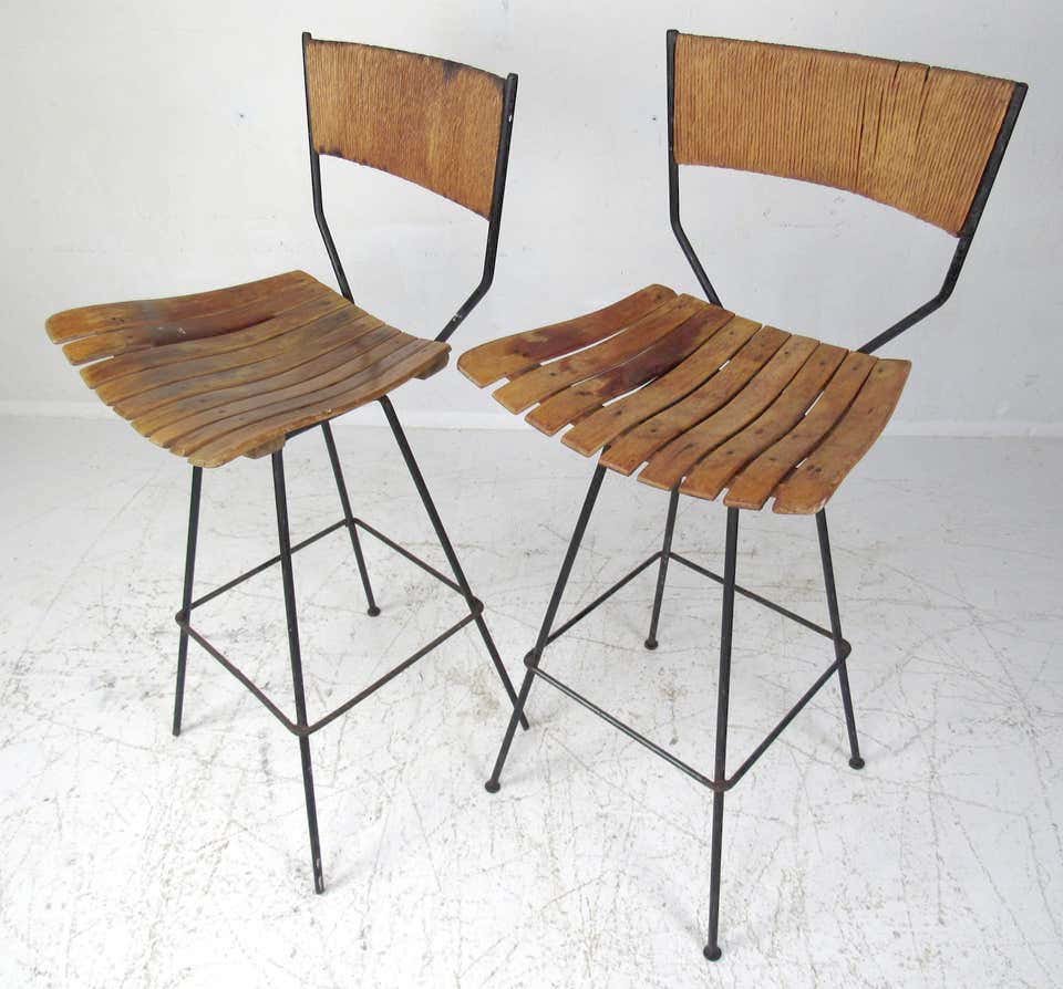 Pair of Arthur Umanoff Swivel Slat Stools: Pair of Arthur Umanoff tall swivel bar stools designed for Raymor in the 1960s. These iconic stools feature an iron base with bentwood slatted seats and a woven rush backrest.---DIMENSIONS: H 41.5 in.