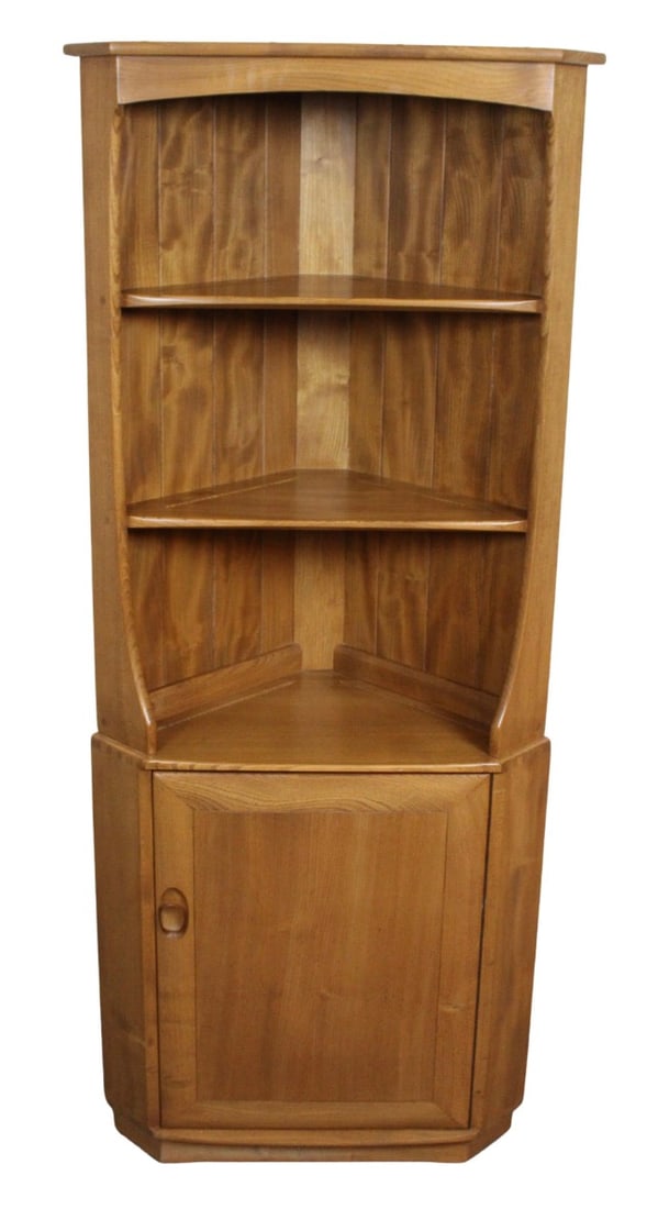 Mid-Century English Elm Corner Cupboard by Ercol: Charmingly chic solid elm triangular corner cabinet manufactured by Ercol of England in the mid-century post-war era. With an impressive 6 foot height, it houses three open shelves atop a single door
