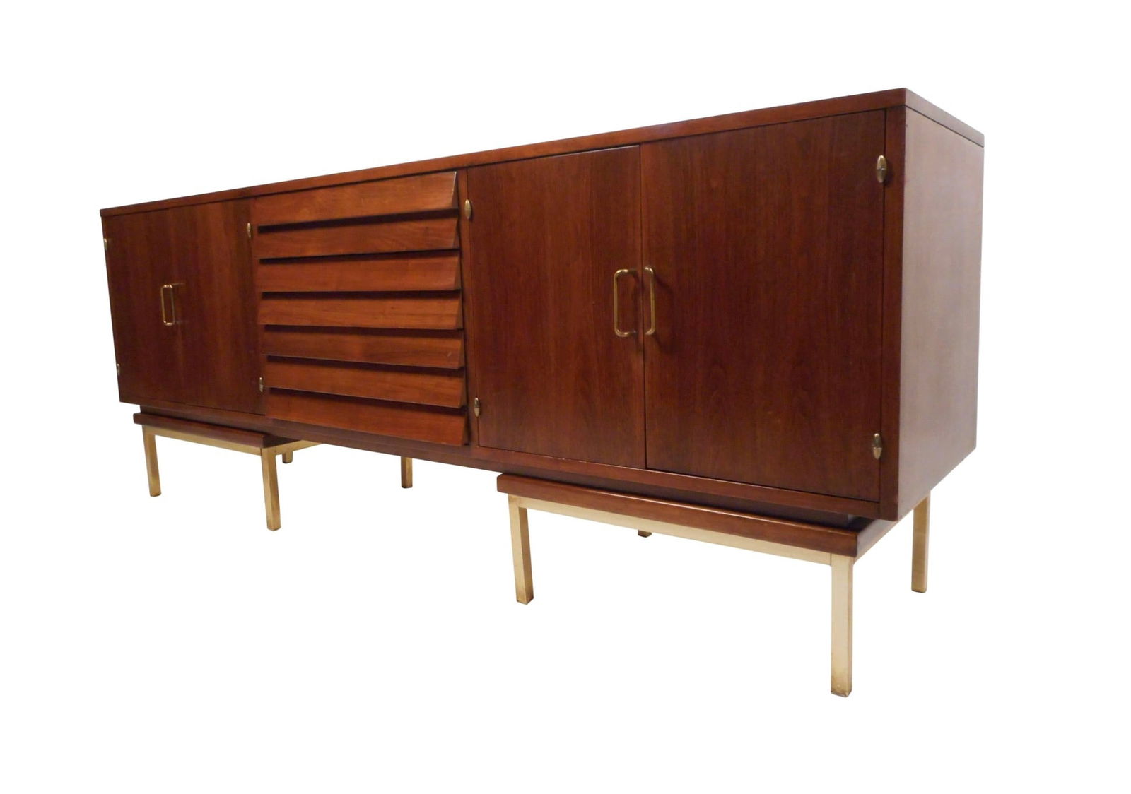 Walnut Credenza by American of Martinsville with a Louvered Front: This massive vintage modern sideboard features three louvered drawers in the middle and two large storage compartments on the sides. The rich walnut finish, sculpted brass handles, and unique brass ba
