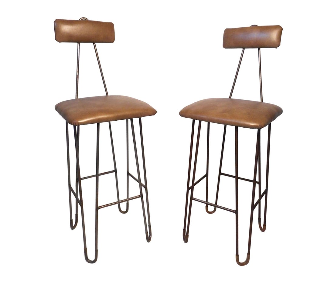 Pair of Mid-Century Stools: These stylish and unusual mid-century stools feature sturdy iron hairpin frames, comfortable seating, and sleek faux-leather upholstery. Angular backrest supports peak above the cushion giving the sto