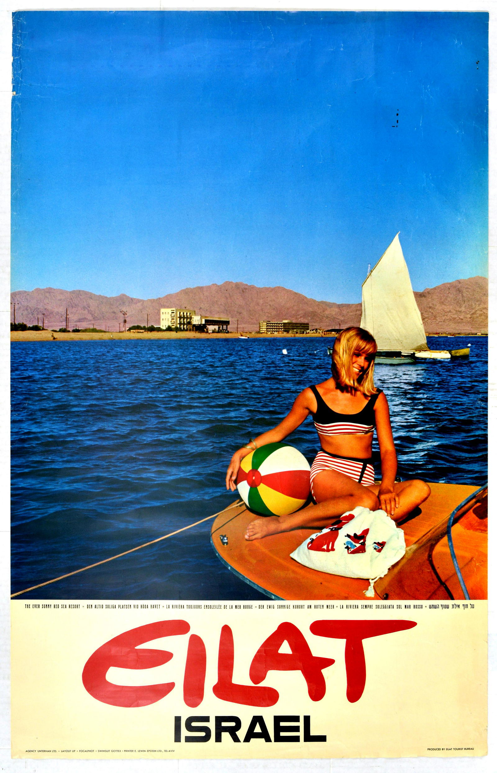 Travel Poster Eilat Israel Red Sea Resort Sailing: Original vintage travel advertising poster for Eilat, Israel, with a photograph of a young woman in swimwear on a yacht in the sea, holding a beach ball, with a sailboat in the background mountains in