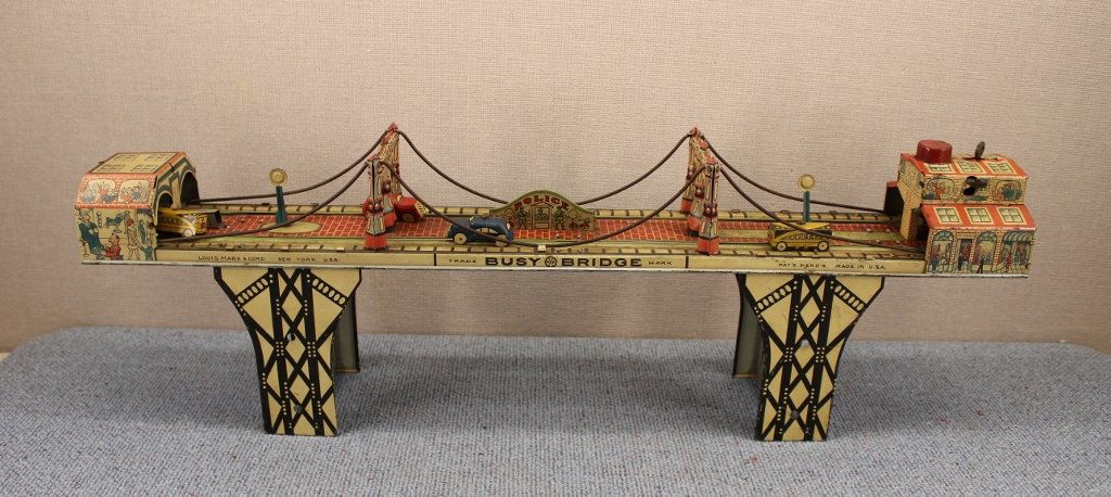 Marx "Busy Bridge" Wind Up Toy ca. 1937: Wonderful tin lithographed Marx toy depicting the Brooklyn Bridge. Wind up clockwork does work. Marked Louis Marx & Comp New York, USA. 24 inches long, 8 inches tall. Five cars, missing the sixth.