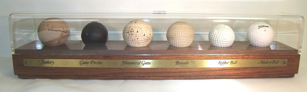 The Evolution of the Golf Ball Showcase: The evolution of the golf ball showcased in a plexiglass case on a wood base. What I can't figure out is why I still can't hit it! For the avid golder or for someone who just wants to be. Appox 17"L x