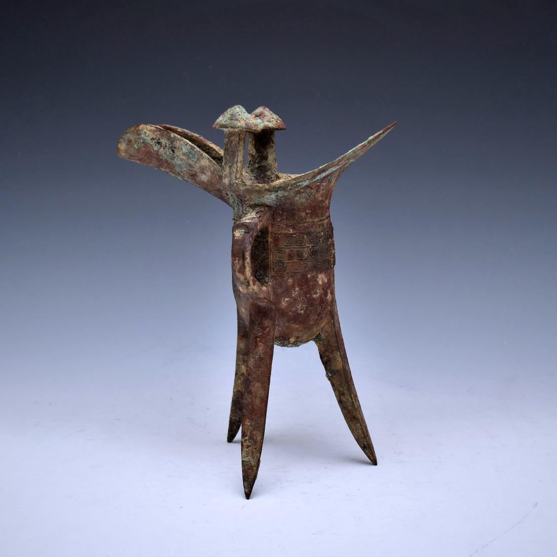 CHINESE BRONZE RITUAL TRIPOD WINE VESSEL, JUE: A CHINESE BRONZE RITUAL TRIPOD WINE VESSEL, JUE PROB. SHANG DYNASTY, 12TH-11TH CENTURY BC The deep body is raised on three blade-shaped supports and is cast on the sides with a band of two taotie mask