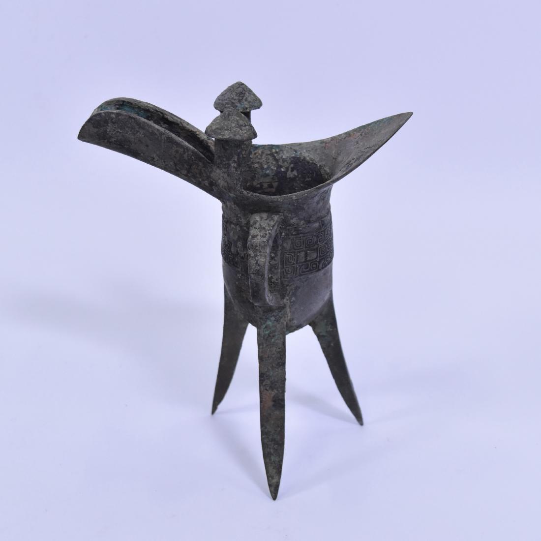 CHINESE BRONZE RITUAL TRIPOD WINE VESSEL, JUE: A CHINESE BRONZE RITUAL TRIPOD WINE VESSEL, JUE PROB. SHANG DYNASTY, 12TH-11TH CENTURY BC The deep body is raised on three blade-shaped supports and is cast on the sides with a band of two taotie mask
