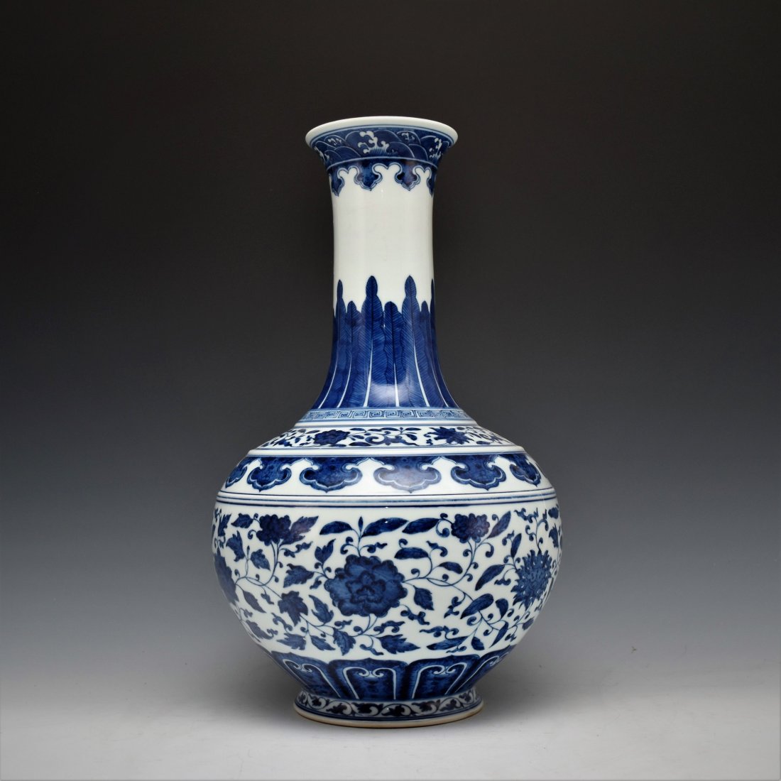 BLUE AND WHITE FLORAL CELESTIAL VASE: Chinese porcelain potted in a celestial form, bulbous body with round shoulder gently tapered toward tall cylindrical neck, leading to slightly wider rim; raised upon a flat concaved base. The exterio