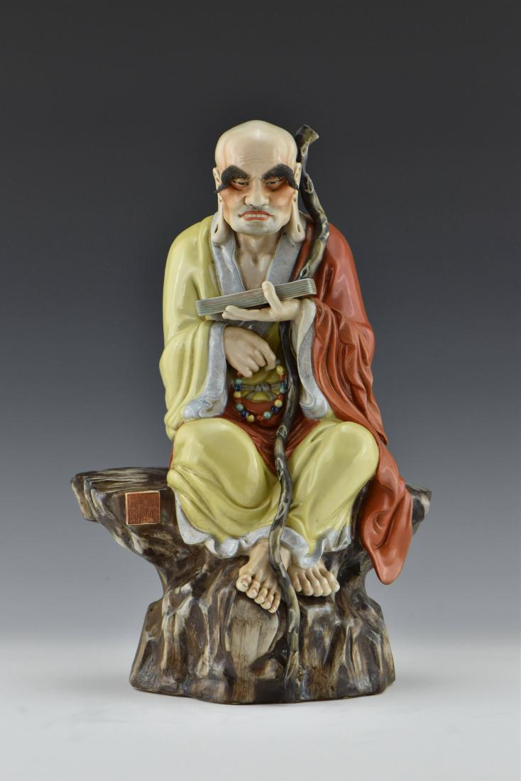 CHINESE FAMILLE ROSE LUOHAN SCLUPTURE: Chinese porcelain finely potted in a shape of seated LuoHan, with thick eyebrow, dressed in a yellow monk robe and red jiasha. Right hand holding a prayer beads bracelet, left hand holds a book. A woo
