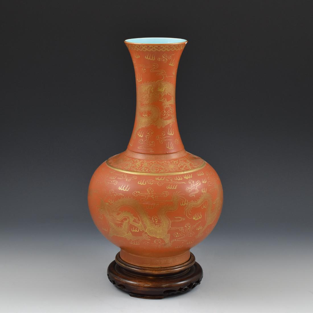CHINESE GILT DRAGON VERMILLION RED VASE ON STAND: Chinese porcelain potted in a celestial form, bulbous body with round shoulder gently tapered toward tall cylindrical neck, leading to flared rim; raised upon a splayed foot base. The exterior delicat