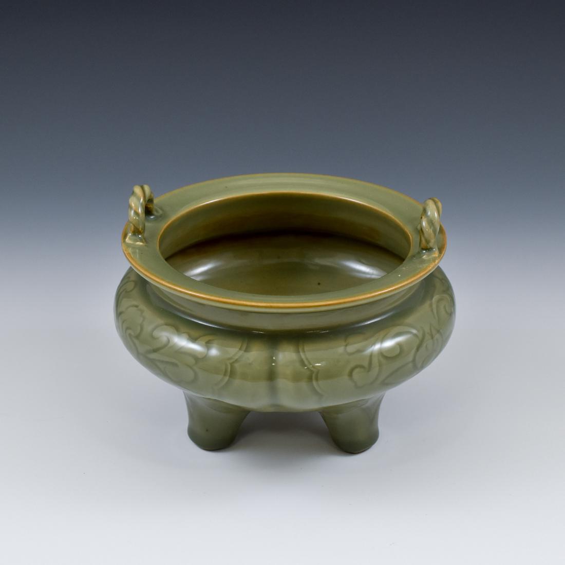 CHINESE LONGQUAN CELADON CENSER: The Chinese porcelain tripod censer sturdily potted in compressed globular body, with three lobed sides radiating toward the broad wide flori-form rim. Raised on three slightly splayed conical support
