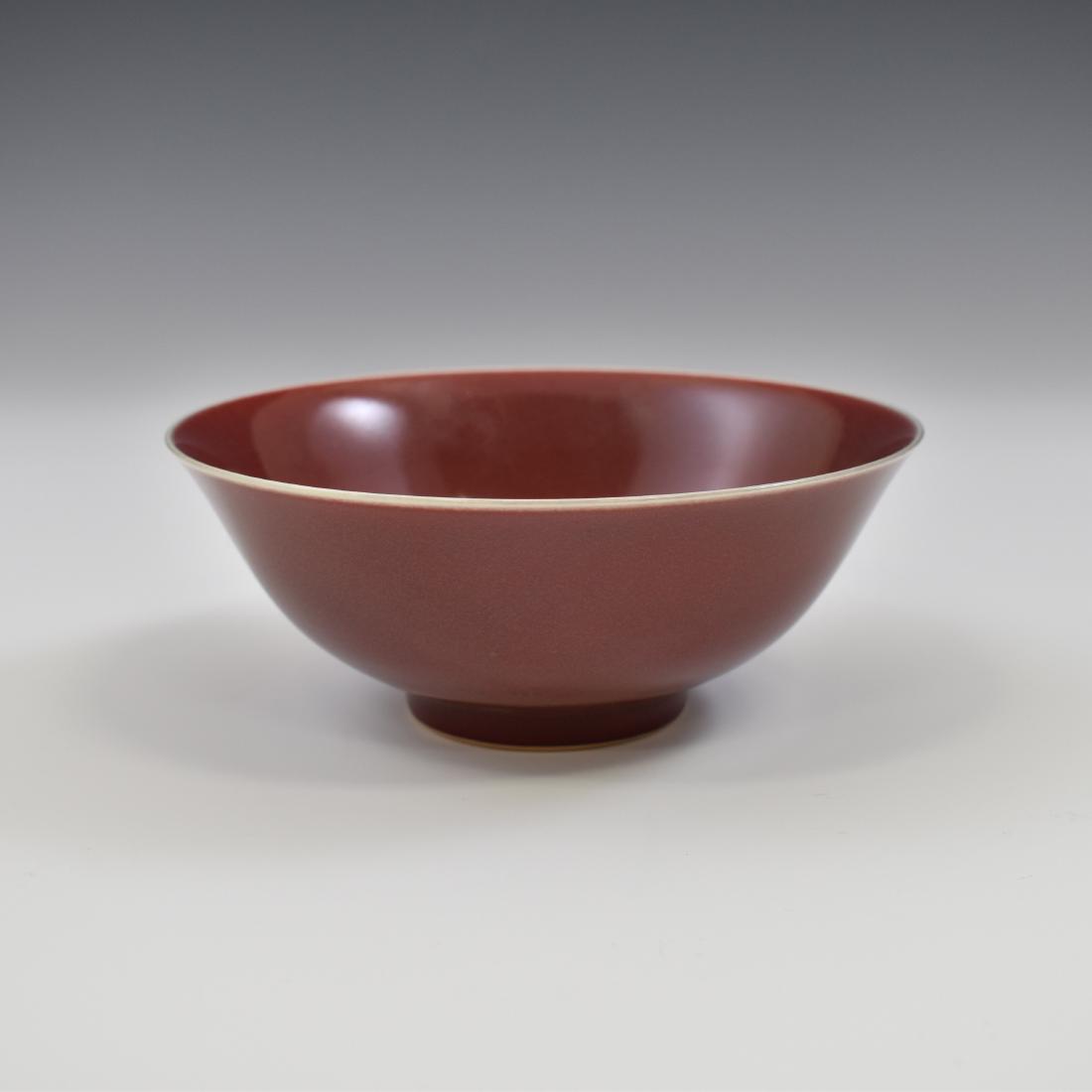 QIANLONG OX BLOOD MONOCHROME BOWL: Deep ox-blood QianLong Chinese porcelain bowl, with red glaze characterized by a blushing effect. Deep curvature flaring upward to form the rim, with a slightly raised footing. Defined by the deep red