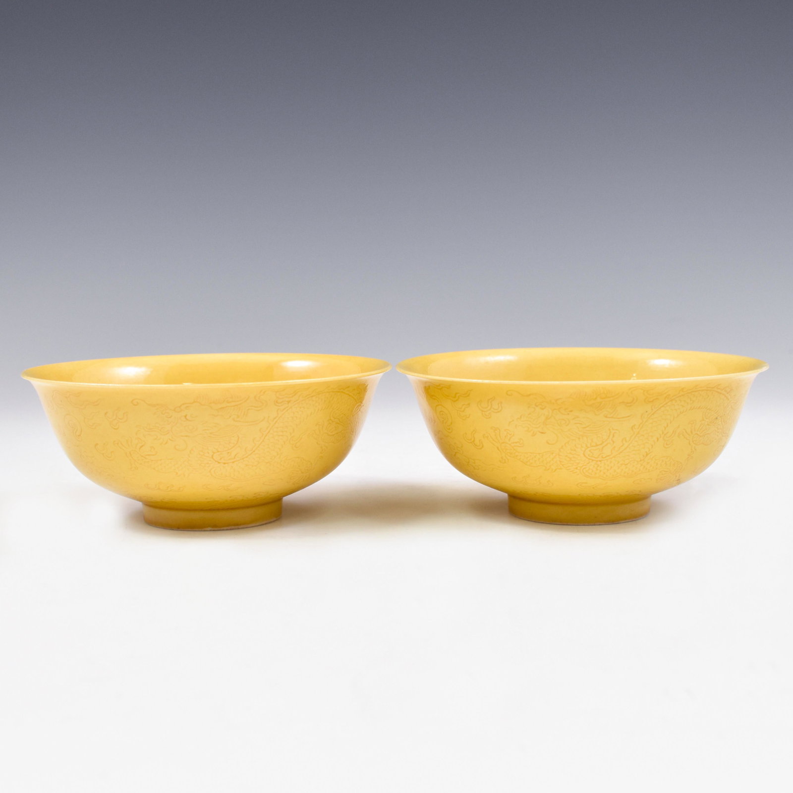 PAIR KANGXI YELLOW MONOCHROME BOWLS: Dimensions: 2" H x 5" Dia. (each) Pair of Chinese Qing Dynasty Period, Kangxi lemon yellow monochrome sgraffito dragon porcelain bowls. The porcelain potted with a shallow body, of a shallow vessel, w