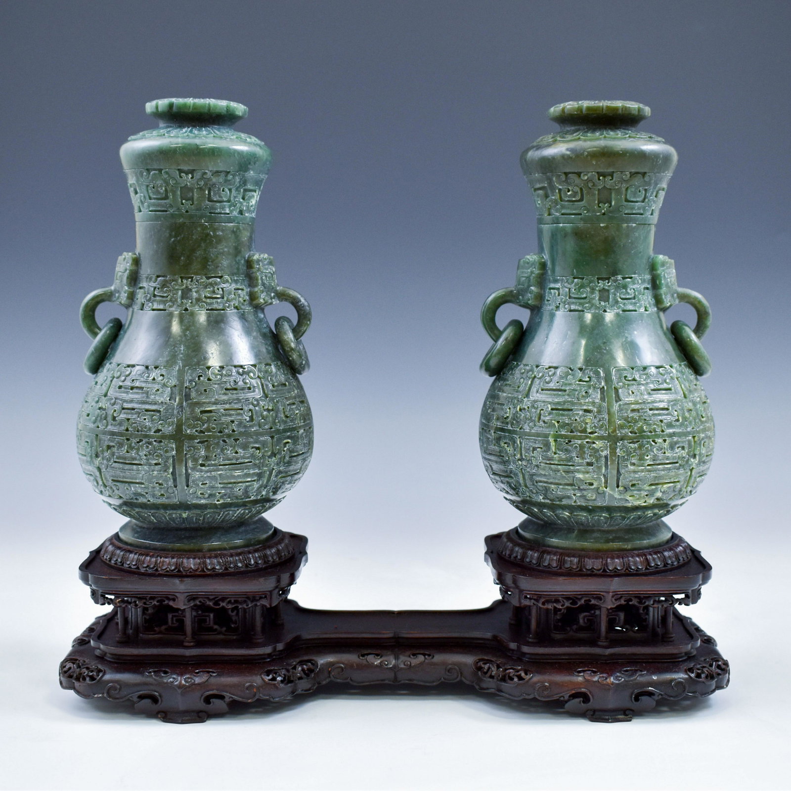 PAIR CHINESE GREEN JADE VASES ON STAND: Elaborate Pair of Spinach-green Jade vases. The exterior decorated in relief with centralized Taotie mask patterns. The taotie mask may be totemic and can resemble protection or be a representation of