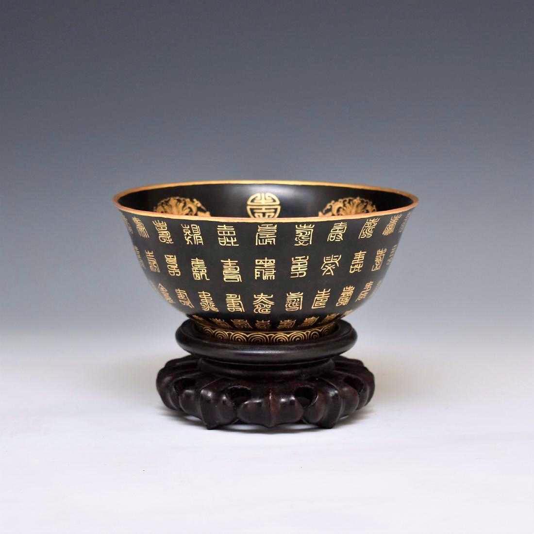 YONGZHENG GILT EBONY LACQUERED BOWL ON STAND: A Qing Dynasty Chinese Lacquered bowl with rounded cavetto rising the steep sides toward slightly lipped rims, raised upon a narrow footed base. The exterior delicately hand wrote with various longevi