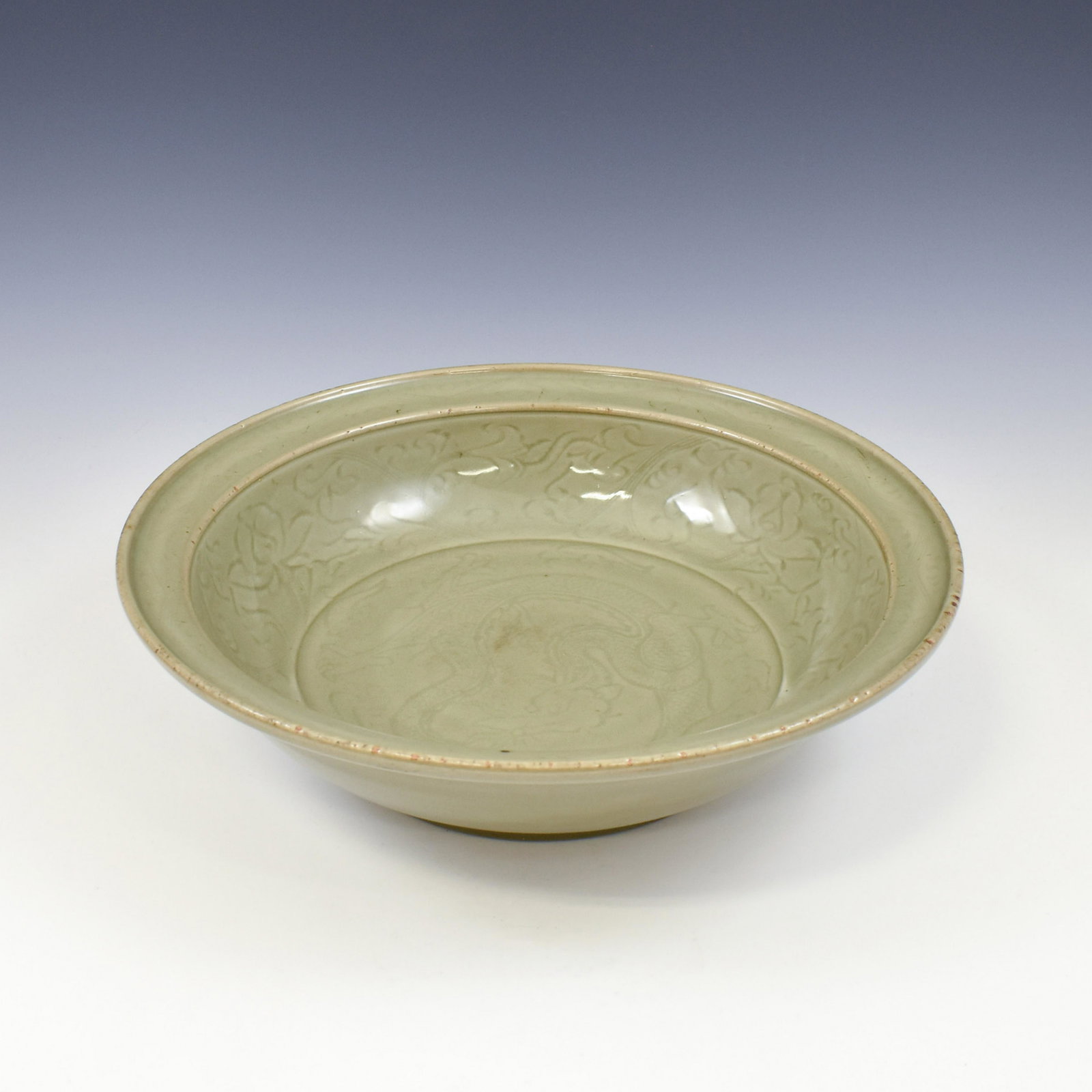 A LARGE CARVED DRAGON MING LONGQUAN CELADON CHARGER: Chinese Ming Dynasty LongQuan celadon charger. Shallow body, with a slightly flared lip with a shallow draft. Centrally festooned with a dynamic dragon soaring amidst flames and vapors. The exterior i