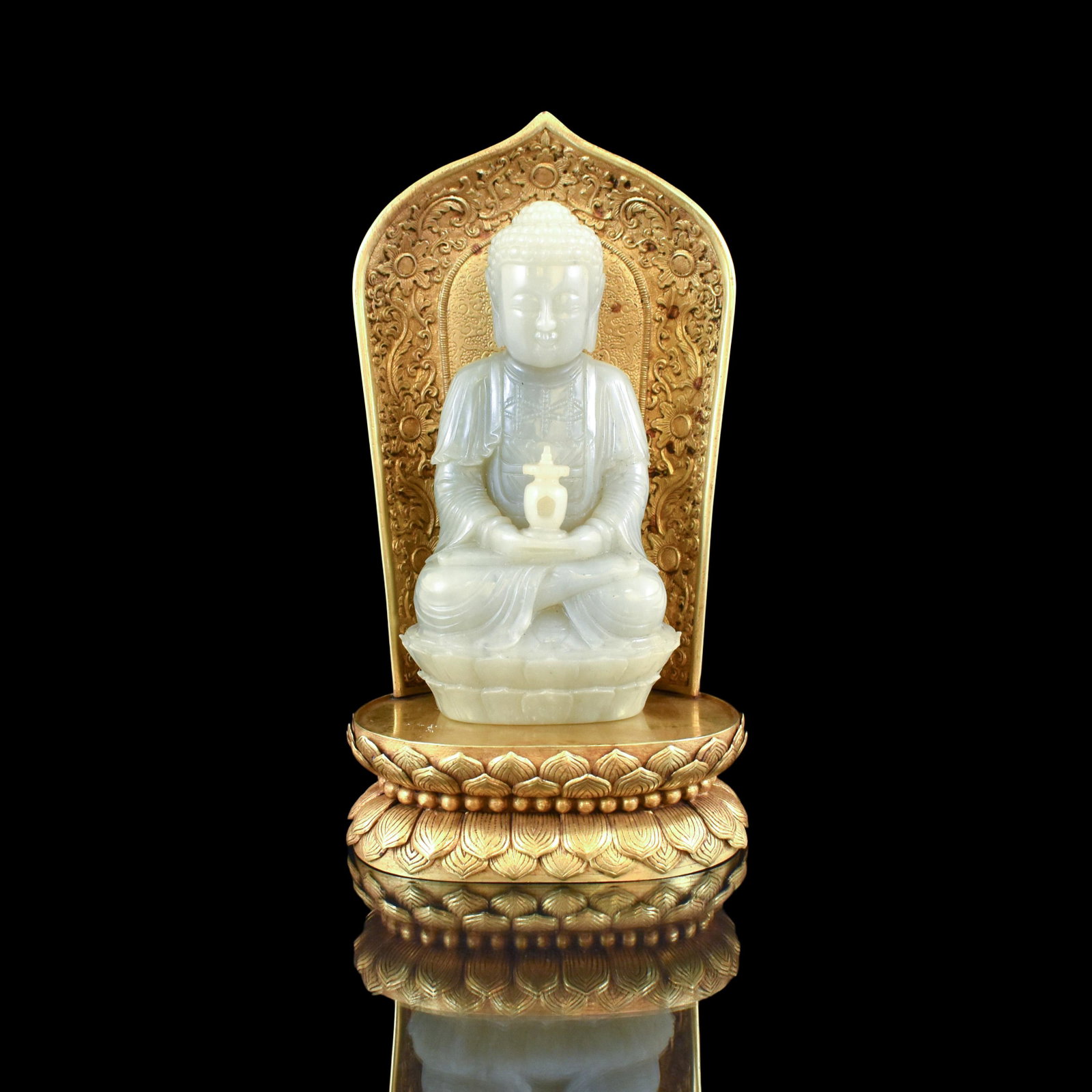 JADE CARVED BUDDHA ON GILT BRONZE AUREOLE & THRONE: Dimensions: Height: 6 1/4" Width: 3 1/2" Stand Height: 8 5/8" Width: 4 3/4" Weight: 896 g A carved Chinese white Jade in form of a Buddha figure, with serene face, closing eyes, and elongated ears ben