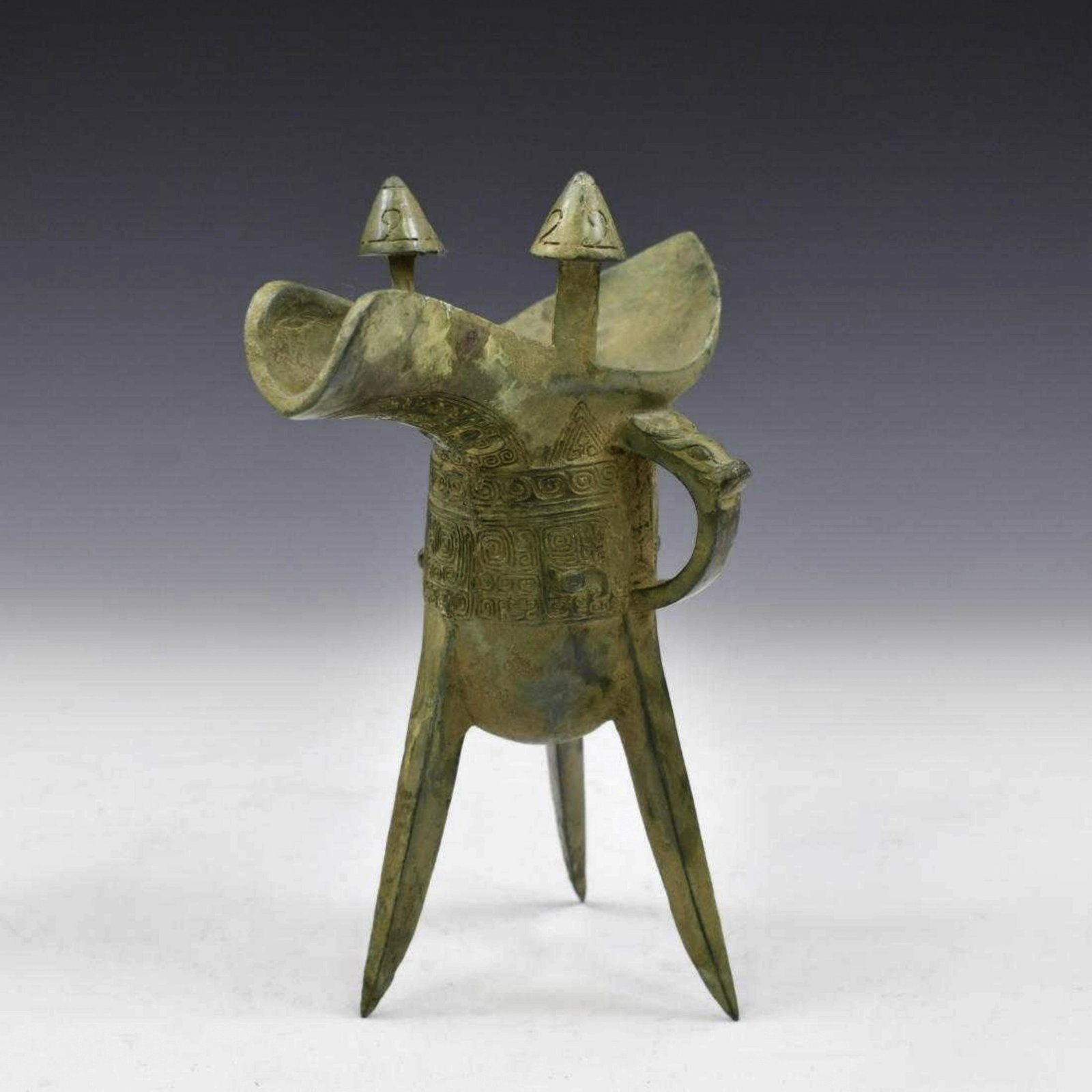 CHINESE ANTIQUE BRONZE JUE WINE VESSEL: Dimensions: 6.5in H x 6in W Antique Chinese bronze ritual Jue wine vessel. The deep body is raised on three blade-shaped supports. Scored geometric patterns line the vessels outer diameter. Taotie mas