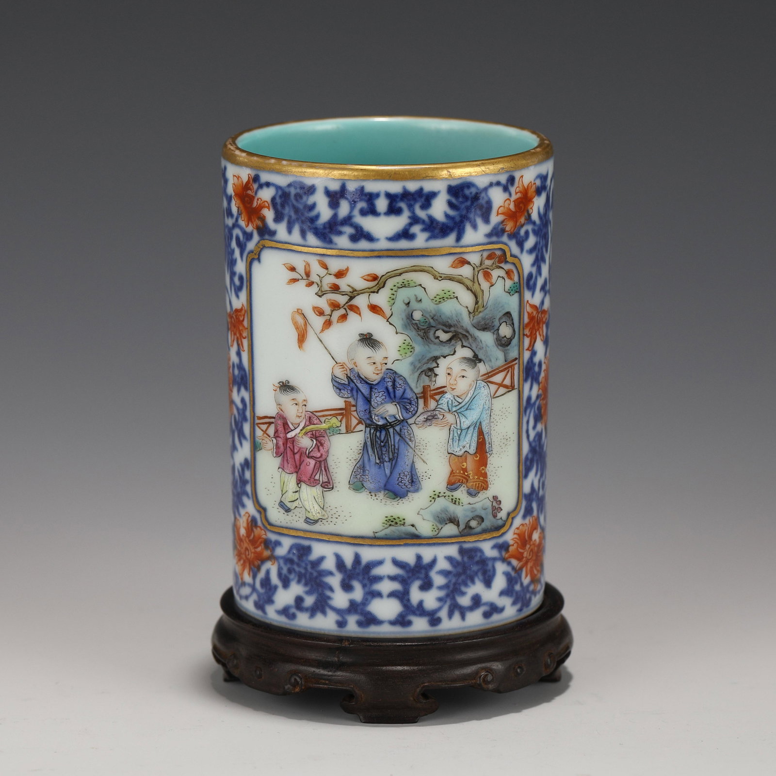 QIANLONG FAMILLE ROSE & GILT BRUSH POT ON STAND: Dimensions: Height: 8.5 cm, Diam.: 5.7 cm Chinese Qing Dynasty Qianlong Famille Rose Young Children Motif Porcelain Brush Pot on Carved Hardwood Stand. The Porcelain potted in brush holder shape, stur