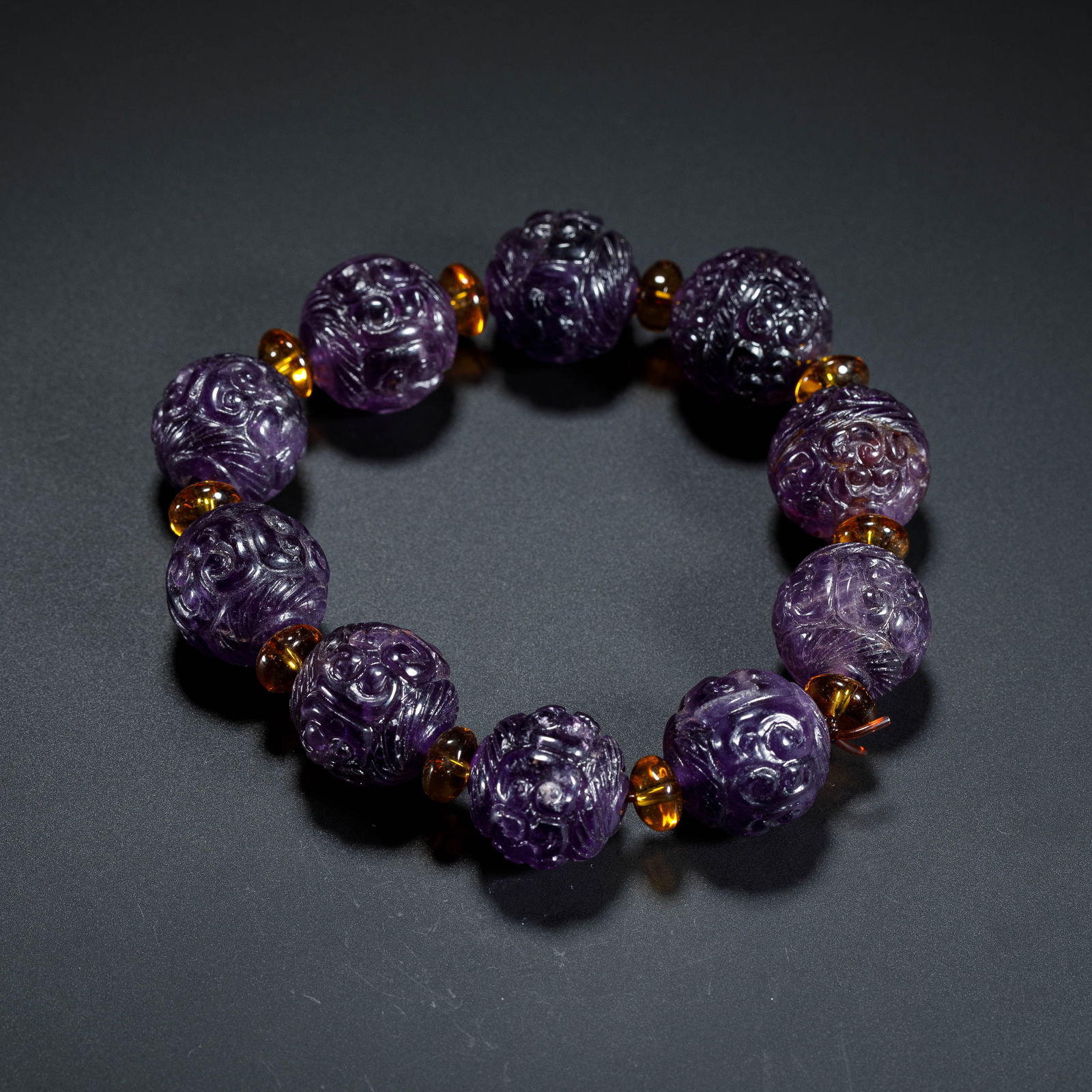 CHINESE AMETHYST BEAD BRACELET: Dimensions: L. 1.9 cm. Weight 82 grams. This elegant Chinese amethyst bead bracelet features ten intricately carved spherical beads, each adorned with scrolling cloud and dragon motifs that