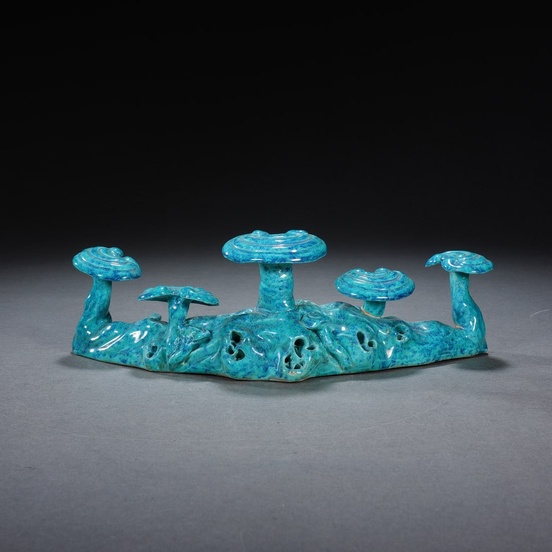 CHINESE BLUE GLAZED LINGZHI BRUSHREST: Dimensions: 19x5x6 cm. A graceful Chinese brushrest, modeled as a gnarled rock formation supporting five lingzhi fungus sprigs, covered in a vibrant, mottled turquoise-blue glaze. The organic form and