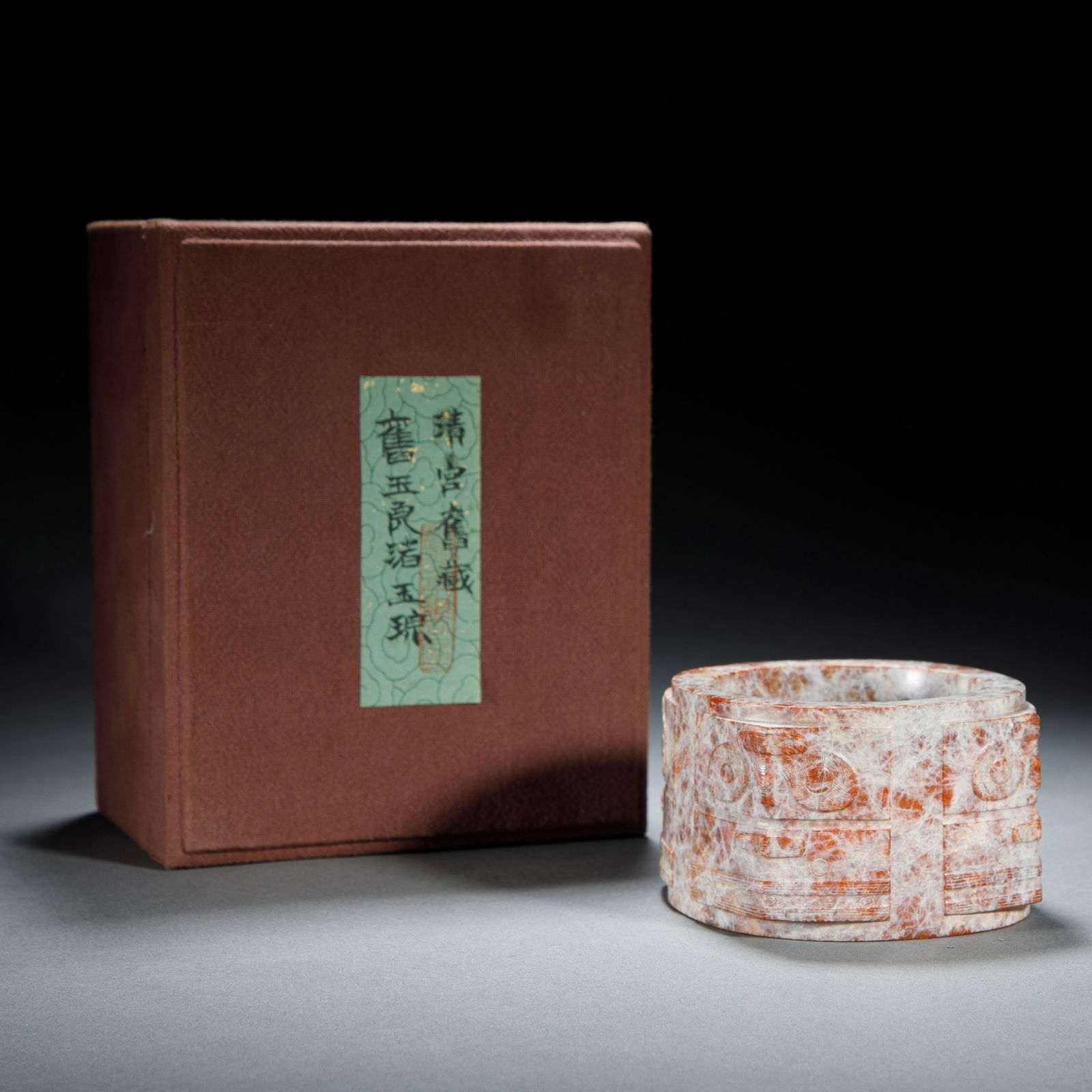 CHINESE HETIAN JADE CONG: Dimensions: L. 7.8 cm. H. 5 cm. This striking Chinese Hetian jade cong features a cylindrical form with squared corners, carved with intricate archaic mask motifs. Its surface displays a