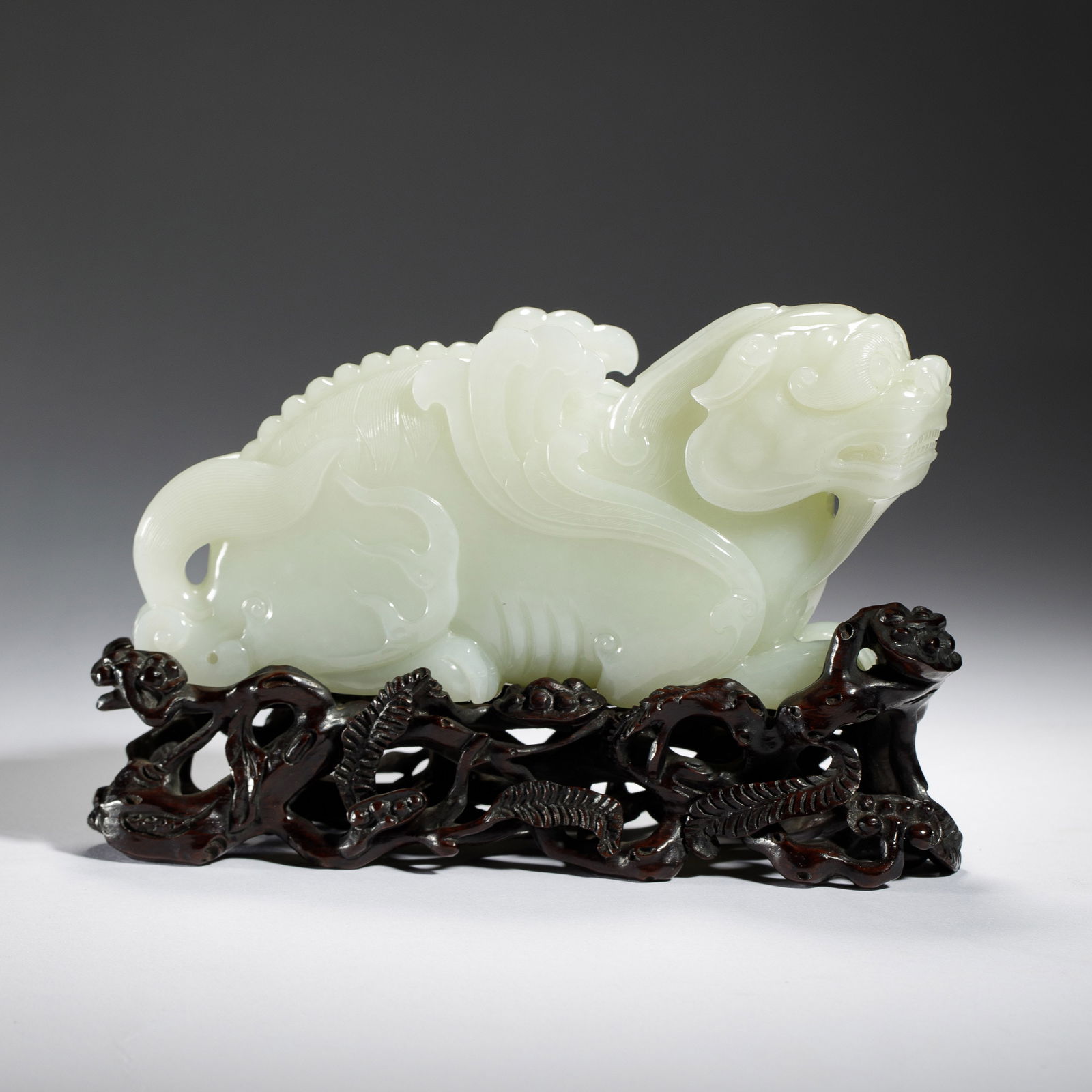CHINESE HETIAN JADE BEAST: Dimensions: L. 17.3 cm. H. 8.6 cm. Weight 1195 grams. This magnificent Chinese Hetian white jade beast is carved in a dynamic, recumbent posture, with a flowing mane, curled tail, and a fierce yet ser