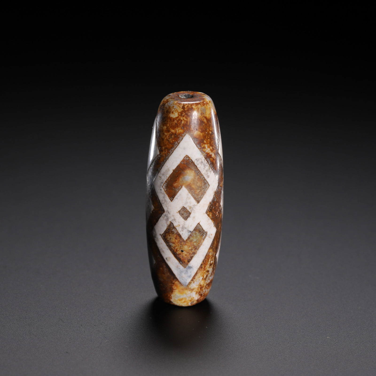 CHINESE DZI BEAD: Dimensions: L. 5 cm. Weight 20 grams. This exceptional Chinese dzi bead features an elongated barrel shape, crafted from agate with a rich, variegated brown and ochre patina. Its surface is adorned wi