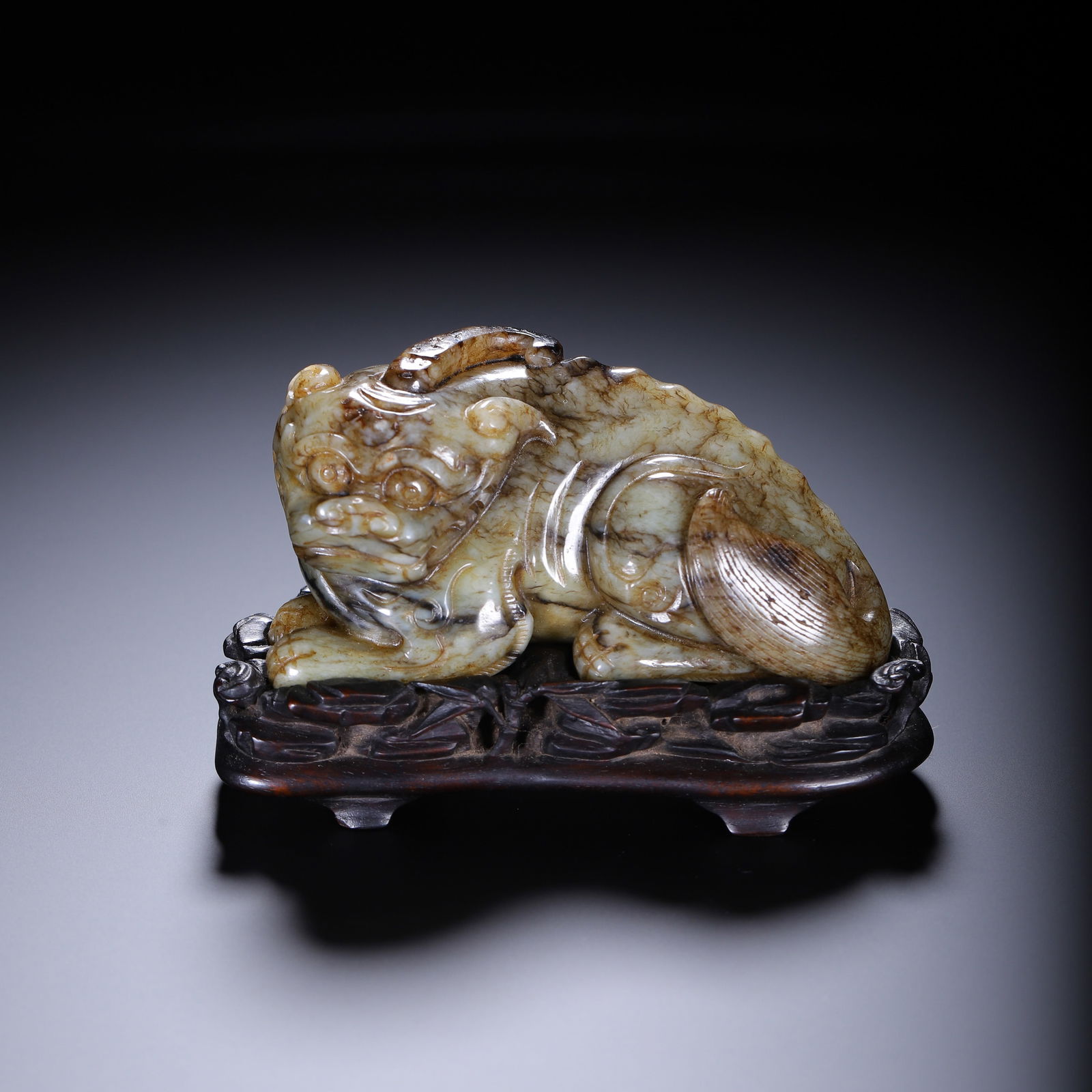 CHINESE JADE MYTHICAL BEAST CARVING: Dimensions: L. 10.5 cm. W. 5.5 cm. H. 6.5 cm. Weight 340 grams. This captivating Chinese carving depicts a mythical beast, rendered from mottled celadon jade with natural russet inclusions. The