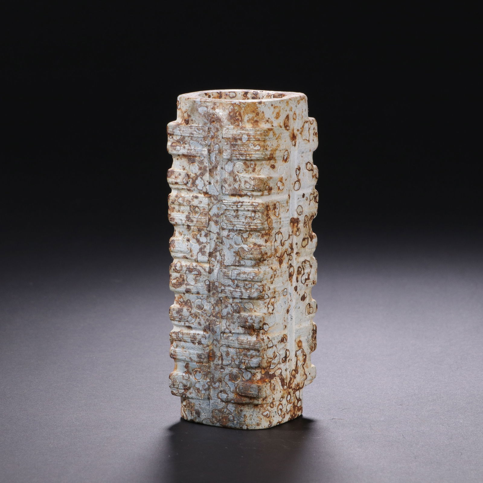 CHINESE JADE CONG: Dimensions: H. 10.3 cm. W. 3.8 cm. This archaic Chinese jade cong features a rectangular prism form with a central perforation, its surface carved with layered, geometric motifs characteristic of anci