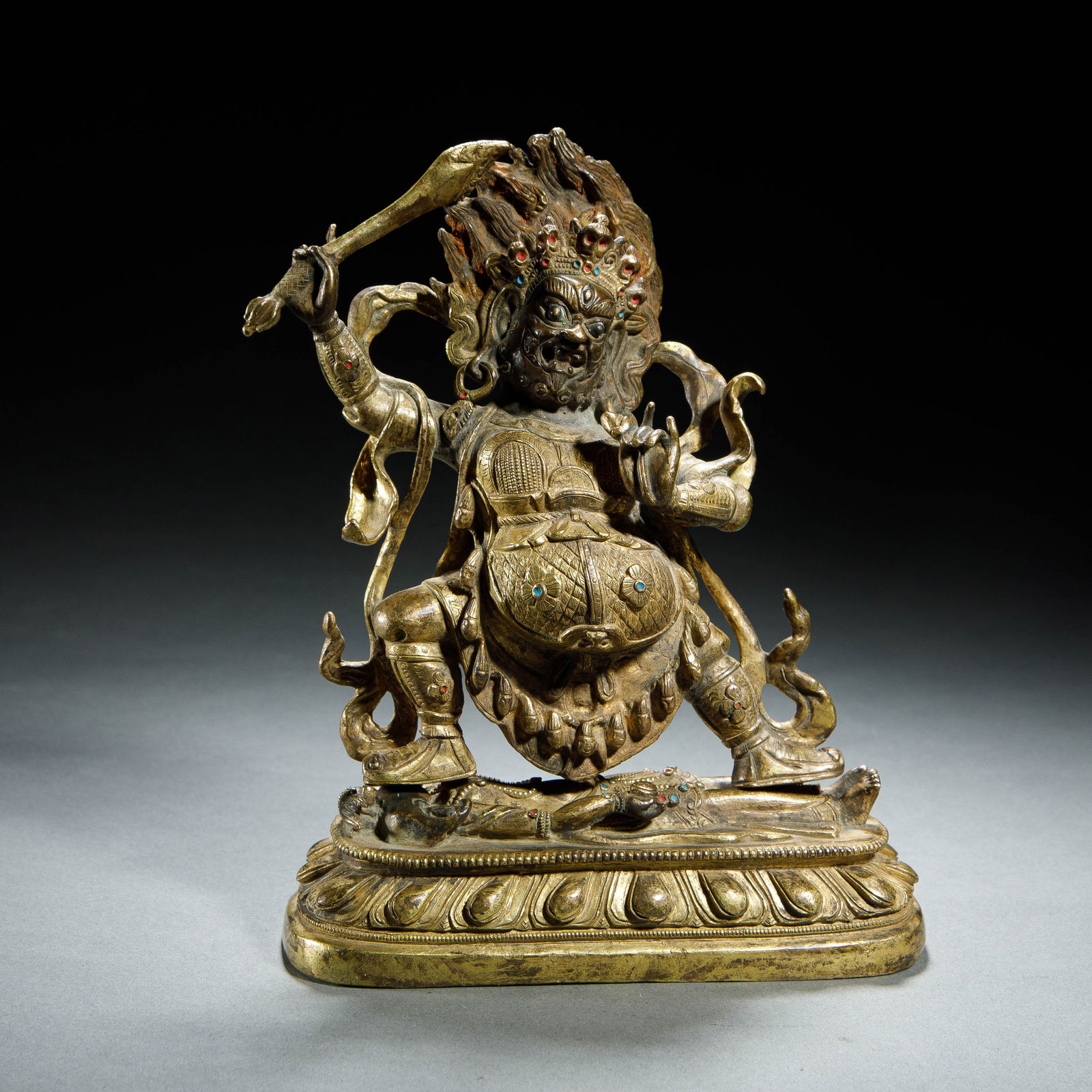 CHINESE GILT BRONZE VAJRA: Dimensions: L. 13.5 cm. H. 18 cm. This dynamic Chinese gilt bronze figure depicts a wrathful Vajra protector, standing triumphantly atop a lotus base over a subdued figure. His right hand brandishes a
