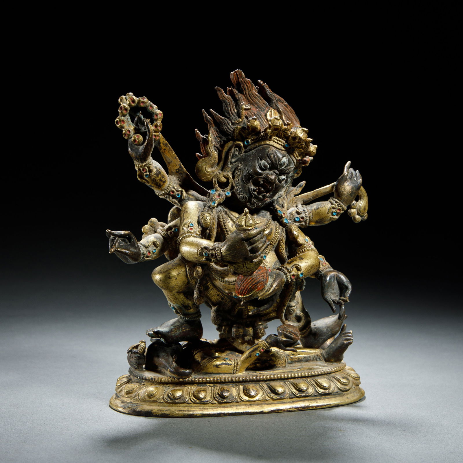CHINESE GILT BRONZE RED-FACED VAJRA: Dimensions: L. 12 cm. H. 18 cm. This powerful Chinese gilt bronze figure depicts the wrathful Red-Faced Vajra, a protector deity with six arms, standing dynamically atop a lotus base over subdued figu
