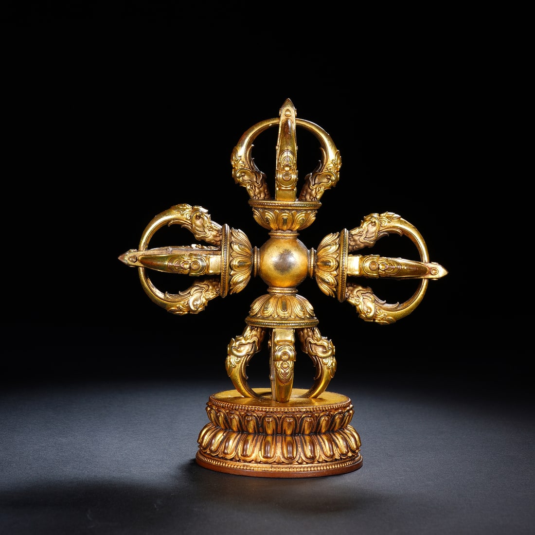 CHINESE GILT BRONZE VAJRA: Dimensions: 13x7x15 cm. Weight 916 grams. This impressive Chinese gilt bronze vajra is presented as a cross-form ritual implement, mounted on a lotus base. Each of its four prongs is adorned with