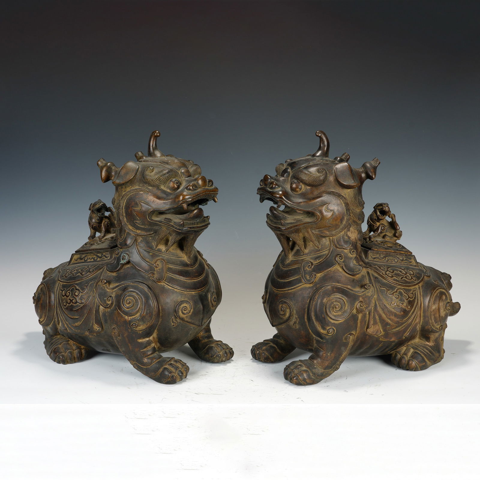 CHINESE BRONZE QILIN CENSERS, PAIR: Dimensions: 38x22x41 cm. A pair of imposing Chinese bronze qilin-form censers, each beast depicted in a recumbent pose with a horned, expressive head, open mouth, and elaborately patterned body.