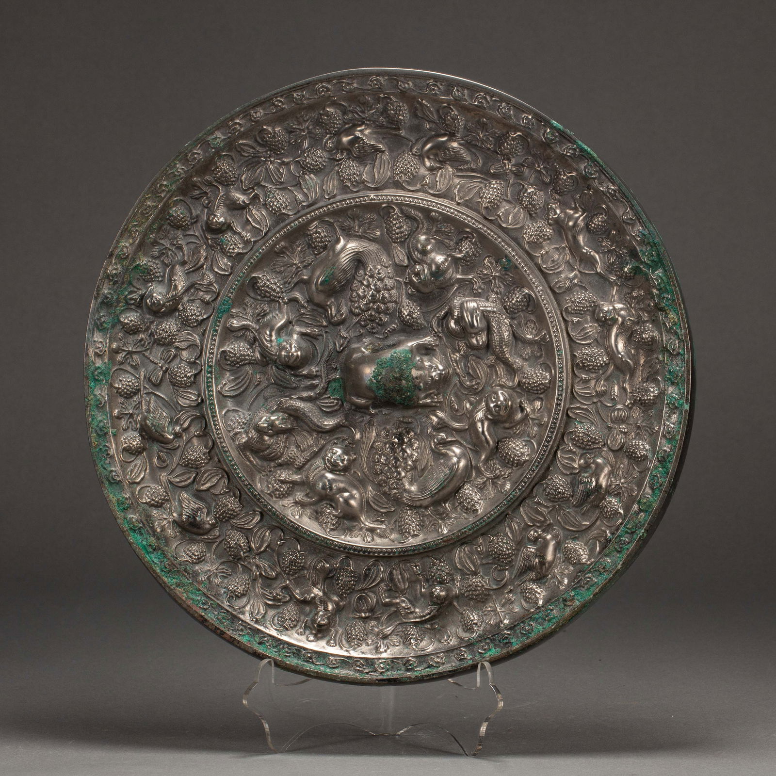 CHINESE BRONZE MIRROR: Dimensions: L. 22.5 cm. W. 22.5 cm. Weight 2560 grams. This exceptional Chinese bronze mirror boasts a highly detailed relief design, featuring mythical beasts, birds, and grapevines that fill both it