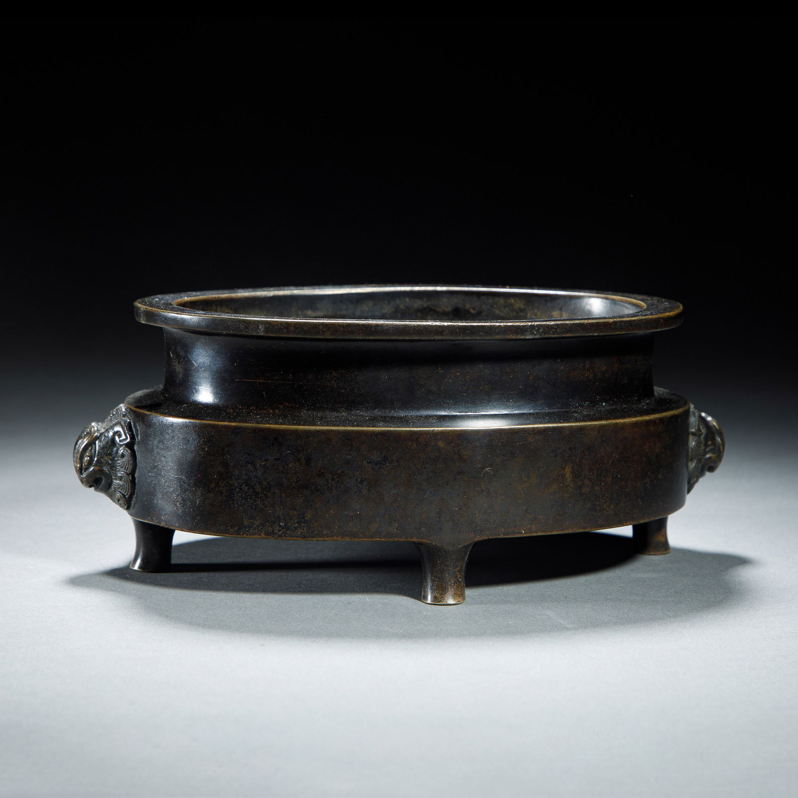 CHINESE BRONZE HORSE TROUGH CENSER: Dimensions: L. 19 cm. H. 8 cm. This elegant Chinese bronze censer features a wide, shallow ?horse trough? form, with a thick, rounded rim and a dark, lustrous patina. It is flanked by two relief lion-