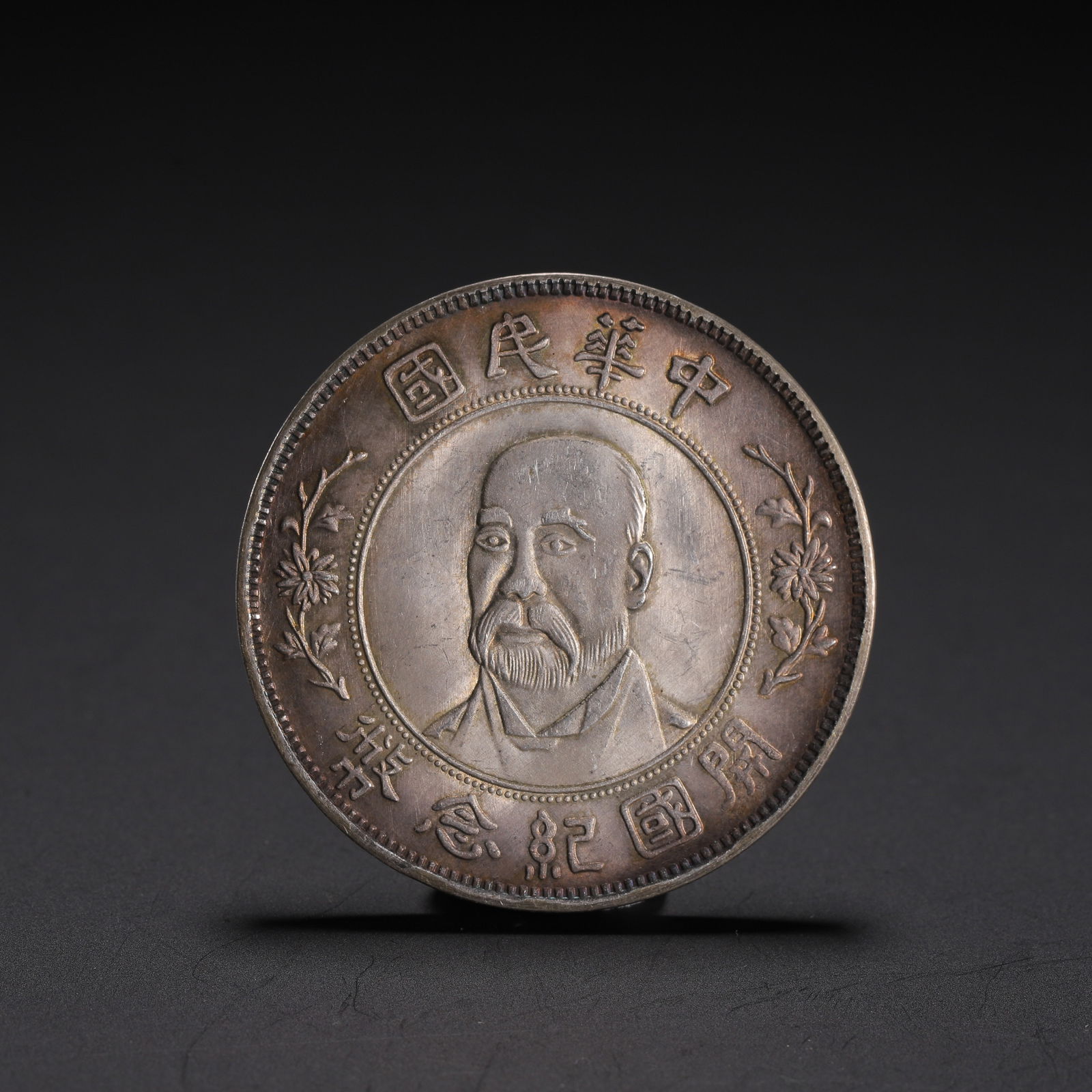 CHINESE SILVER COMMEMORATIVE COIN: Dimensions: L. 4 cm. W. 4 cm. Weight 30 grams. This fine Chinese silver commemorative coin features a portrait of a statesman at its center, framed by floral sprigs. The rim bears the inscription ????