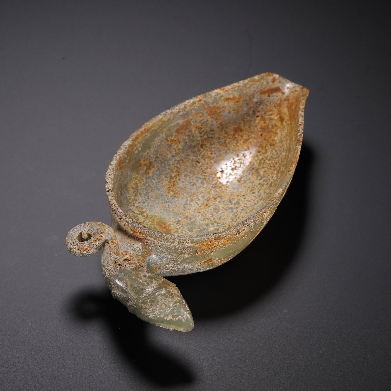 CHINESE ARCHAIC JADE LIBATION CUP: Dimensions: L. 13.5 cm. W. 7 cm. H. 3.5 cm. Weight 150 grams. This elegant Chinese archaic jade libation cup is carved from pale celadon stone with a natural iron-patina surface, featuring a