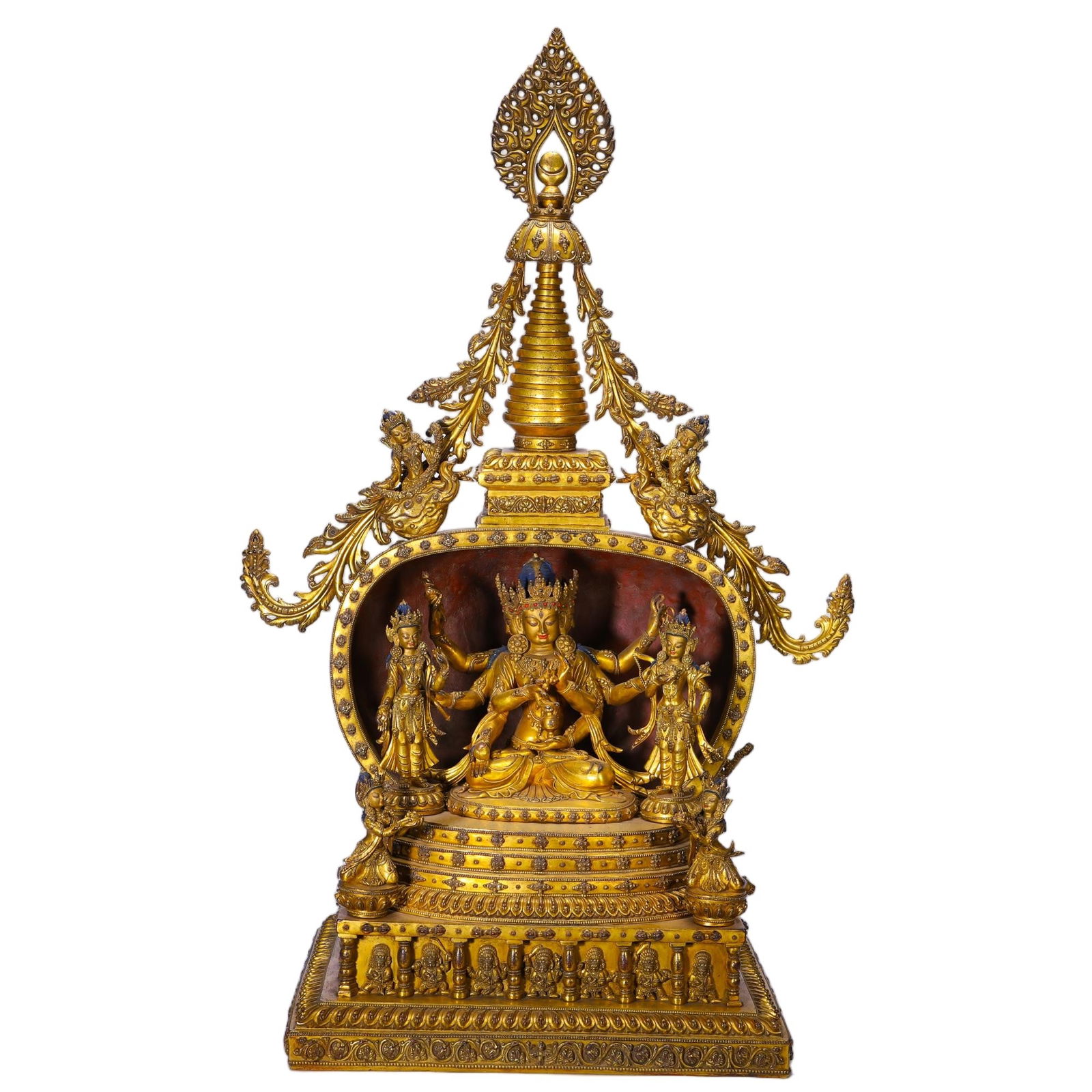 CHINESE GILT-BRONZE SHRINE: Dimensions: L. 46 cm. W. 29 cm. H. 74 cm. This magnificent Chinese gilt-bronze shrine features a multi-tiered, ornately carved structure crowned by a stupa, framing a central multi-armed deity in
