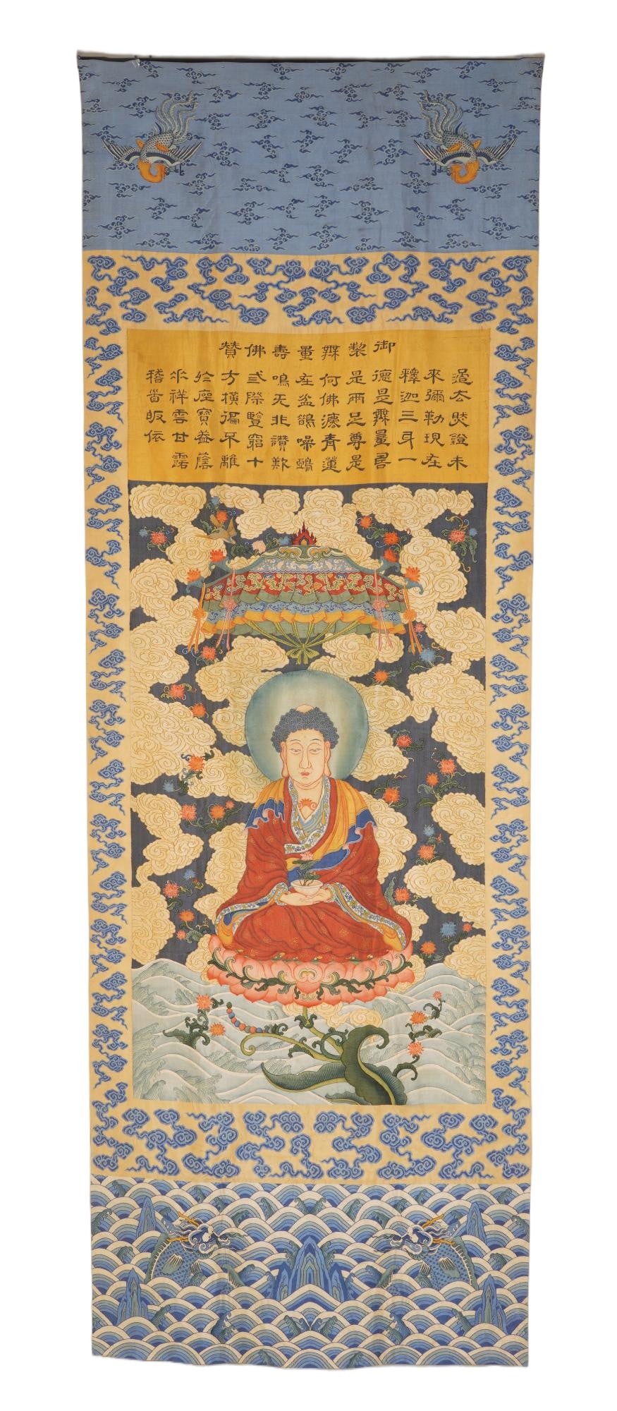 A CHINESE KESI BHAISAJYAGURU THANGKA: Measuring 67 x 146 cm, this vertical kesi-woven thangka showcases Bhaisajyaguru seated serenely upon an ornate lotus throne encircled by billowing cloud scrolls and scattered blossoming flora. A radia
