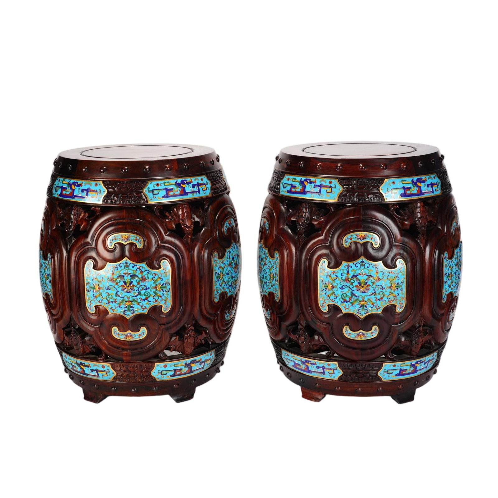A PAIR OF CHINESE ZITAN ENAMEL DRUM STOOLS: This harmoniously matched pair of barrel-shaped drum stools is masterfully crafted from polished dense zitan hardwood. The wooden bodies feature elegant openwork carvings framed by scrolling raised mo