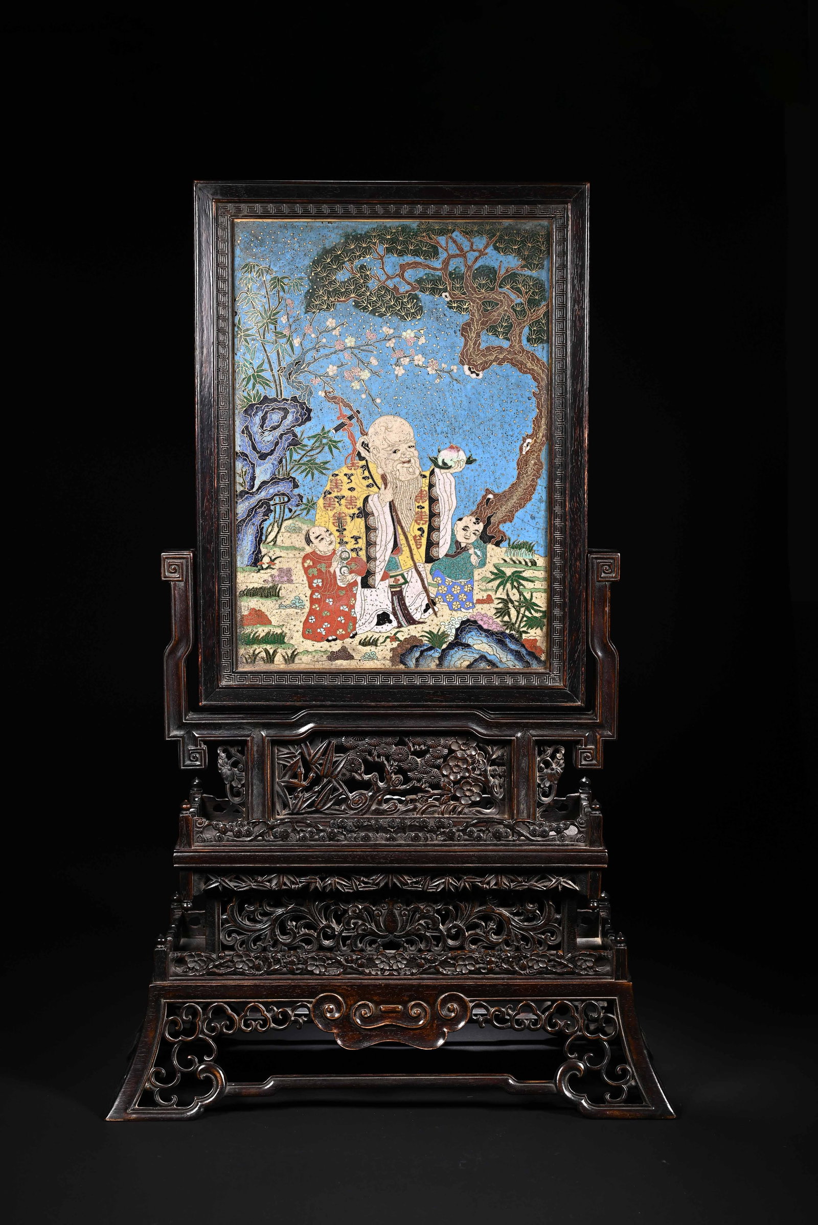 A CHINESE ZITAN CLOISONNE TABLE SCREEN: Standing 57 cm tall and 35 cm wide, this elaborate table screen is mounted in a precisely carved zitan hardwood frame and intricately wrought stand. The stand features layered openwork reliefs of blos