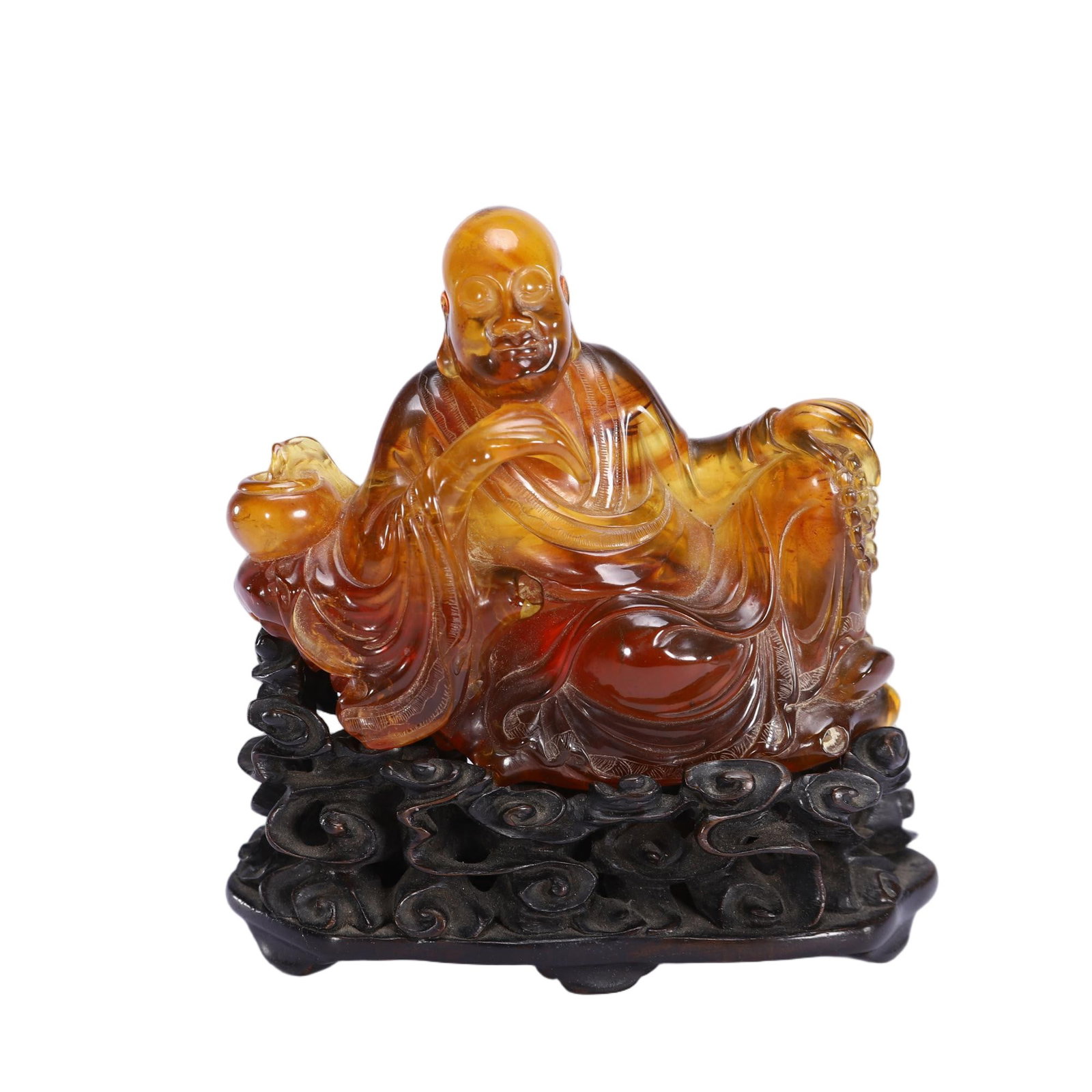 A CHINESE AMBER LUOHAN ORNAMENT: Weighing 160 grams and standing 11 cm in height, this appealing carving is fashioned from translucent amber displaying warm gradients of honey gold and deep reddish-brown tones. The relaxed Luohan set