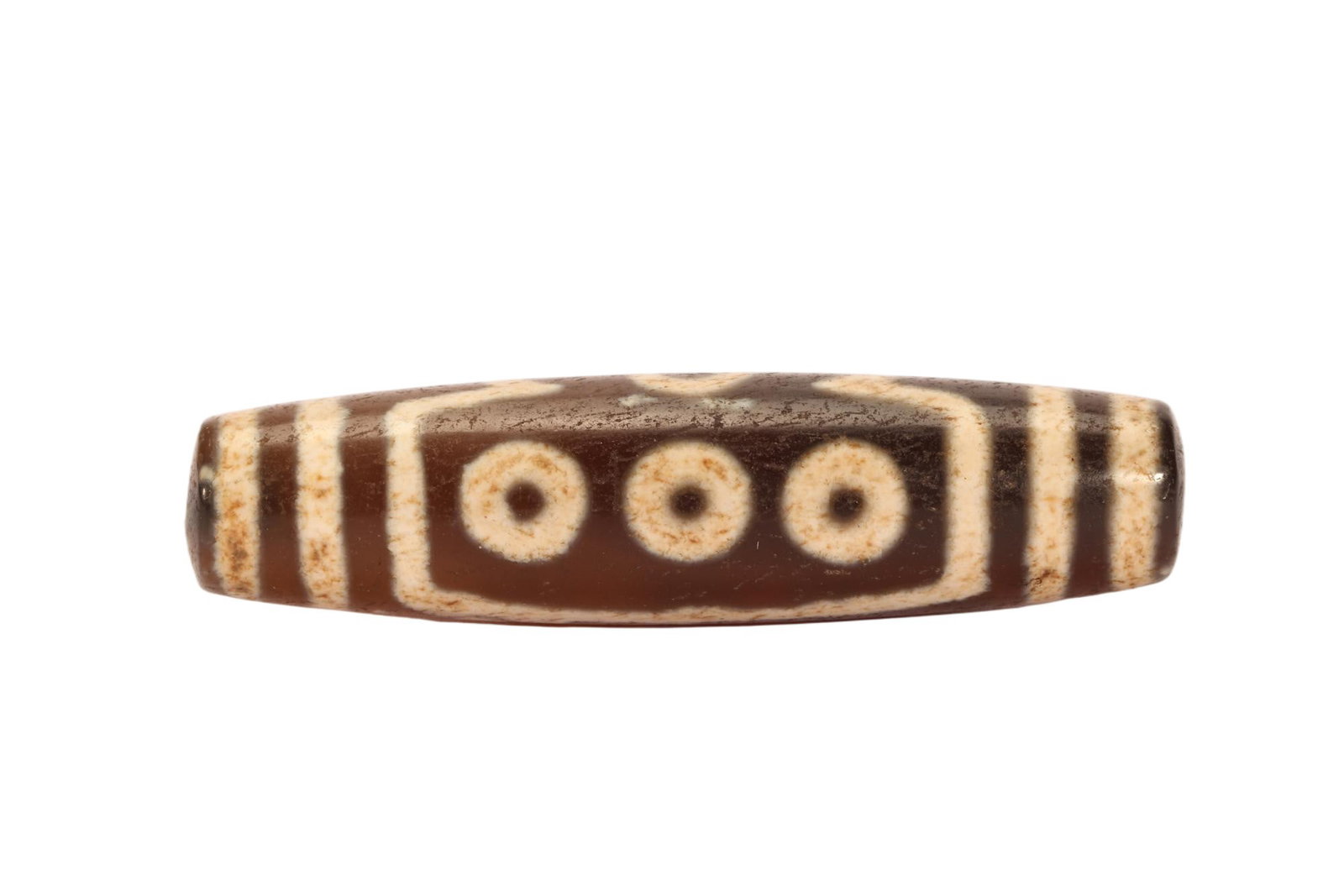 A CHINESE THREE EYE DZI BEAD: Measuring 6 cm in length and weighing 20 grams, this elongated cylindrical dzi bead features a polished deep brown agate base adorned with distinct creamy etched motifs. Three neatly aligned circular 